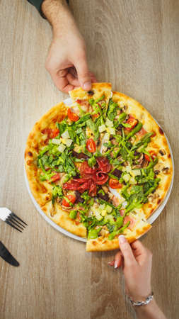 four hands taking pieces of pizza top view on the background of a wooden table