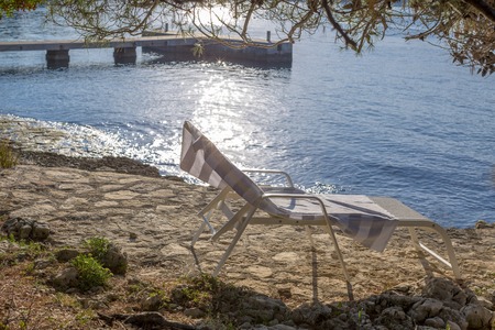 Empty lounger on the rocky beach with blue sea backgroundの写真素材