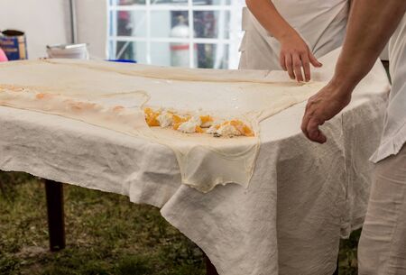 Homemade strudel dough on a traditional linen tablecloth ready for making cottage cheese pie and other pastry. Women roll up the dough with tablecloth. The process of making pie dough according to the traditional Hungarian recipe.の写真素材