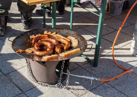 Frying sausages and tasty pieces of lard on an outdoor barbecue propane disc cookerの写真素材