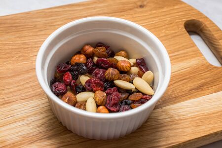 Mixed nuts with cranberries and raisins in white bowl on cutting boardの写真素材