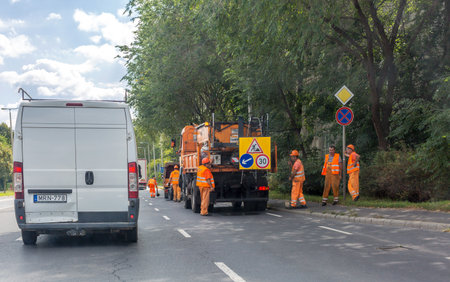 Nyiregyhaza, Hungary â September 06, 2017: Orange car and brigade road repair workers in orange suits on the highway. Asphalt road workers repairs roadのeditorial素材