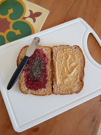 Preparing a whole wheat bread sandwich with peanut butter, blackberry jam and chia seeds filling
