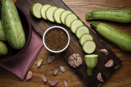 zucchini cut into slices on wooden board with garlic and seasoningsの写真素材