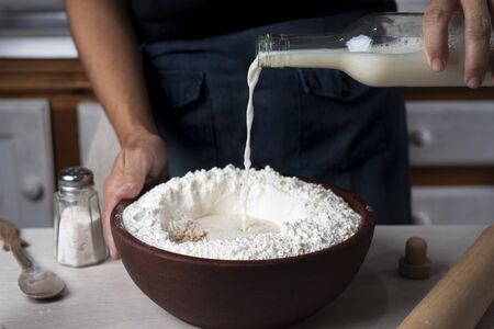 milk falling into wooden bowl with flour and dough ingredientsの写真素材