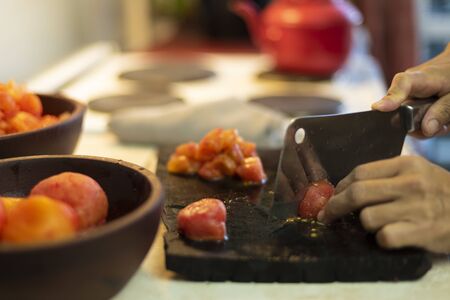 hands cutting tomatoes on wooden board with bowls full of tomatoesの写真素材