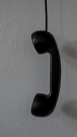 Black telephone receiver hanging on a white wall with copy space for text