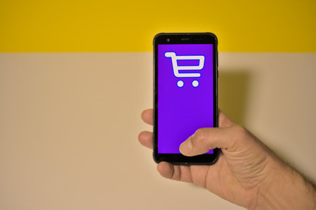 Closeup of hand holding smartphone with shopping cart icon on screenの写真素材