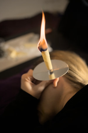 Fair-haired, fair-skinned woman cleans her ears with wax ear cones to remove an earwax plugの写真素材