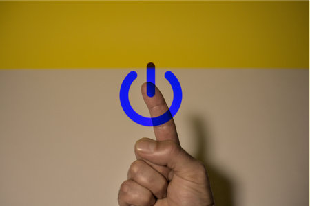 Hand pressing a power button on a yellow and blue background. Power buttonの写真素材