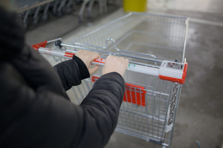 Hand holding shopping cart in supermarket. Selective focus on hand.の写真素材