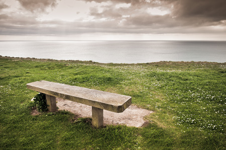 A stone bench by a cliff with sea viewの写真素材