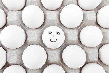 Smiley egg in a box full of white eggs