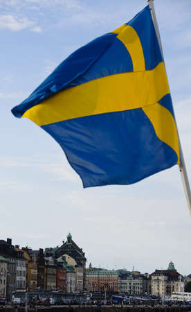 The yellow cross of Swedish flag waving over the buildings of Stockholm old townのeditorial素材