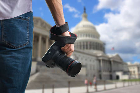 Young man holds black modern digital camera on natural backgroundの写真素材