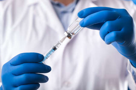 Doctor hand holds syringe and vaccineの写真素材