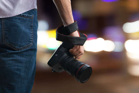 Young man holds black modern digital camera on natural backgroundの写真素材