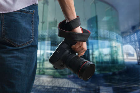 Young man holds black modern digital camera on natural backgroundの写真素材