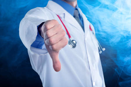 Young doctor with a stethoscope shows bad sign with his handsの写真素材