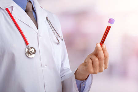 Young doctor with a stethoscope shows tube with blood or plant on pastel gradient backgroundの写真素材
