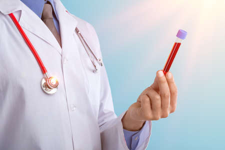 Young doctor with a stethoscope shows tube with blood or plant on pastel gradien backgroundの写真素材