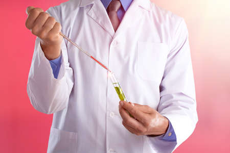 Young doctor with a stethoscope shows tube with blood or plant on pastel gradien backgroundの写真素材