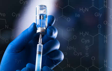 A medical hand in a glove holds an ampoule with a vaccine and a syringe with illustrationの写真素材
