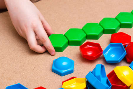 Child's hands stack colored mosaic details in a row on a table. Leisure of the child in confinement....
