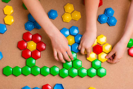 Childrenâs hands put the details of colored mosaics into a drawing of flowers on the table. Leisure of the child in confinement. The development of creative abilities. Top viewの写真素材