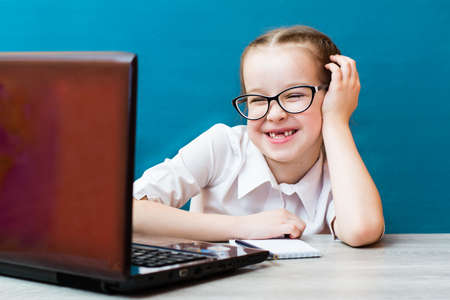Smiling girl in glasses works at a laptop at the table. Distance learning for children. Teleworkの写真素材