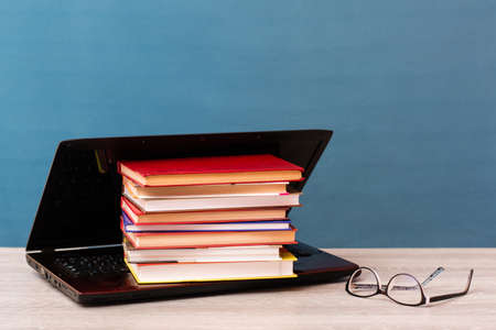 A stack of books lies in an open laptop and glasses on the table. Distance learning. The concept of choosing classical education before modern technologiesの写真素材