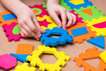 The child's hands put the item in a color puzzle with details of different geometric shapes on the table. Leisure of the child in confinement. Table gameの写真素材