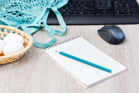 The concept of online shopping without leaving home. Notepad for a shopping list on the background...
