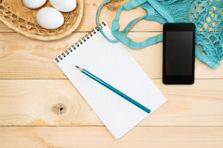 The concept of online grocery shopping without leaving home. Notepad for shopping list, basket with...