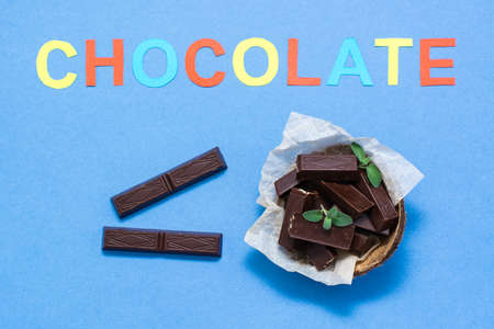 Chocolate pieces and mint leaves in a bowl and the inscription "chocolate" on a blue cardboard background. The concept of excess weight from sweets. Top viewの写真素材