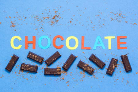 Pieces of chocolate and the inscription chocolate sprinkled with cocoa powder on a blue cardboard...