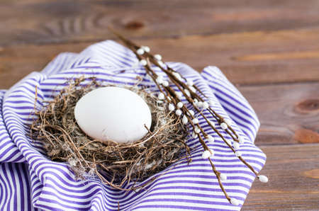 Happy easter. One white chicken egg in a bird's nest and willow branches on a wooden table. Rustic style. Copy spaceの写真素材