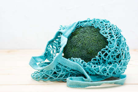 Fresh raw broccoli wrapped in reusable string bag on a natural wooden table. Healthy lifestyle, nutrition and zero waste concept. Copy spaceの写真素材