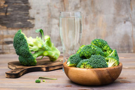 Ready to eat fresh raw broccoli is divided into inflorescences in a wooden plate and on a cutting board  on a wooden table. Healthy lifestyle, nutrition and zero waste conceptの写真素材