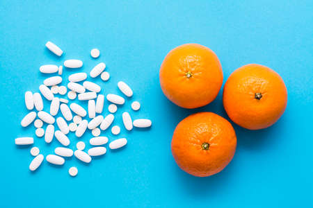 White large oval pills and ripe oranges on a blue background. Medicines and synthetic vitamins. The concept of choosing medicines and natural fruits. Top viewの写真素材