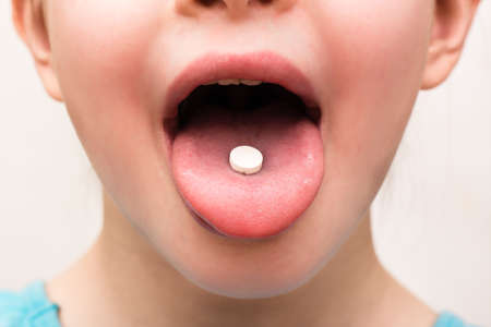 A white round tablet lies on the tongue of a child. Medicines and synthetic vitamins. The concept of drug selection. Treatment for children.の写真素材