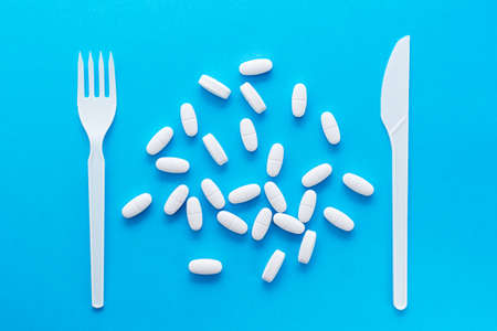 White oval pills and knife with a fork on a blue background. Top view. Uncontrolled use of drugs in large quantities.の写真素材