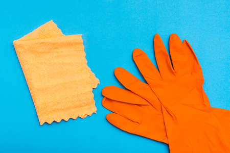 Orange rubber gloves and a yellow microfiber rag on a blue background. The concept of protecting the skin of the hands from chemicals for cleaning.の写真素材