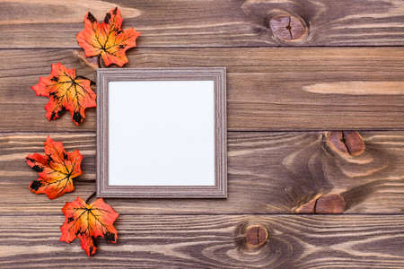 Ready mock up blank photo frame on brown wooden background surrounded by orange maple leaves. Copy spaceの写真素材