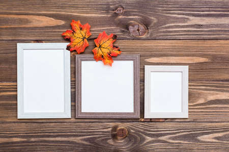 Ready mock up three empty photo frame on a brown wooden background and orange maple leaves. Copy...