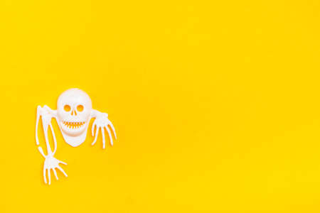 White plastic skull with bones on a yellow cardboard background. Ready Halloween illustration. Copy spaceの写真素材