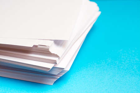 A stack of clean white paper on a table on a blue background. Blank pages ready for printing and writing.の写真素材