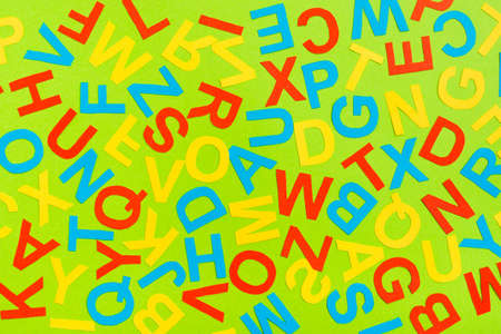Multicolored letters of the English alphabet cut out of cardboard laid out randomly on a green...