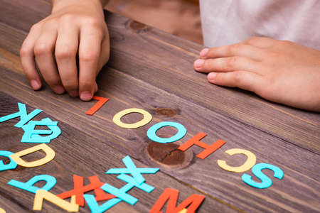Children`s hands make up the word "school" from colored carved cardboard letters on a wooden backgroundの写真素材