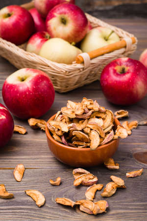 Sliced dried apples in a bowl and fresh apples on a wooden tableの写真素材